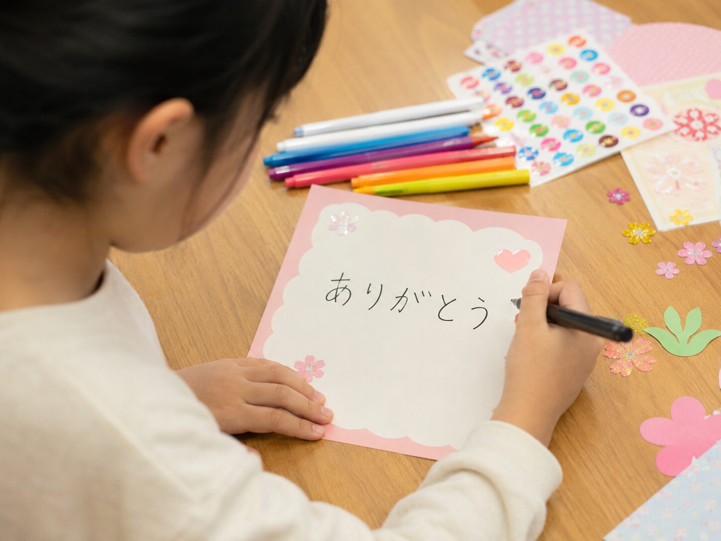 子どもが先生へ渡す寄せ書きカードにありがとうと書いている写真