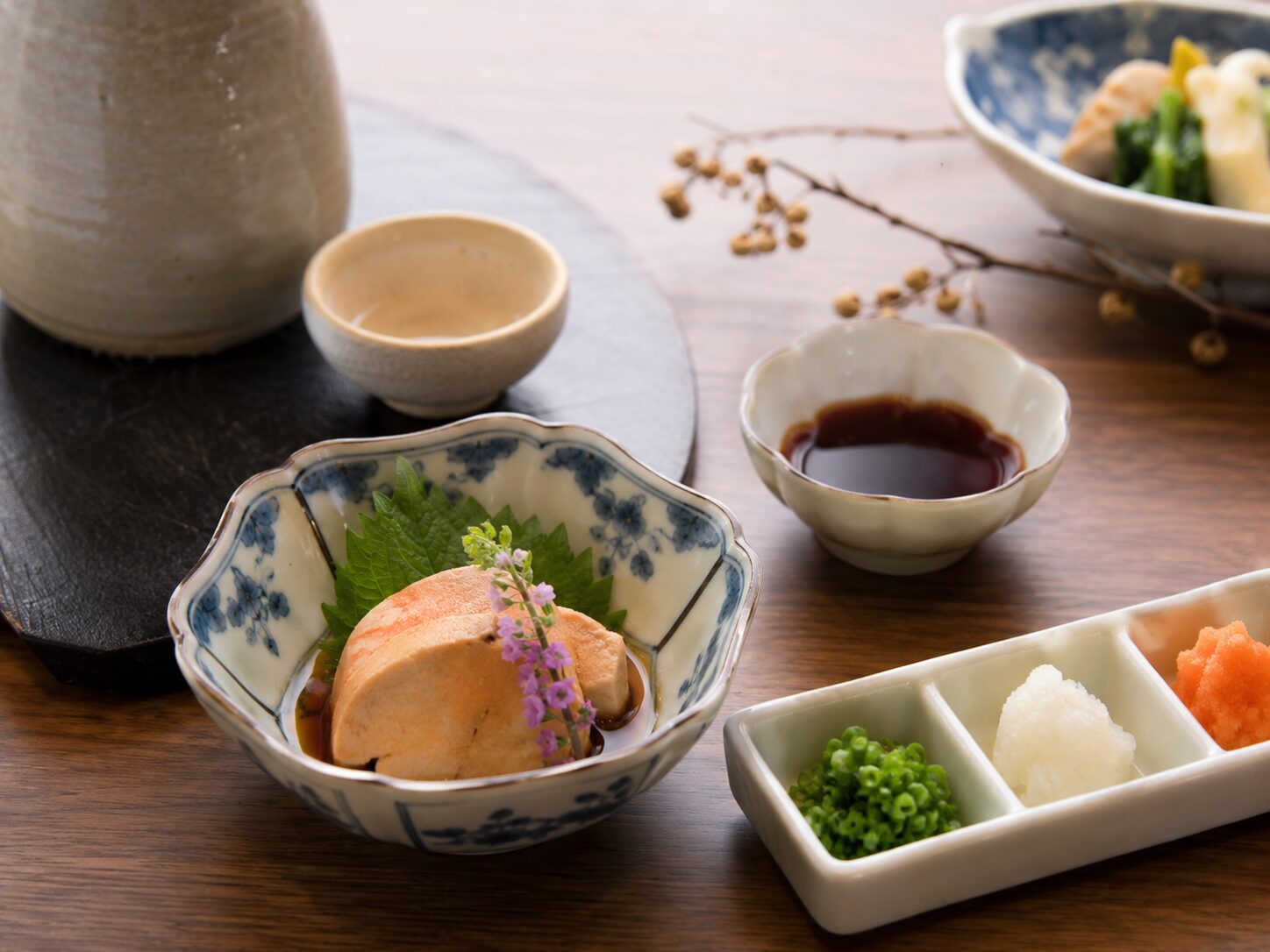 小皿に盛られたあん肝をポン酢と薬味で少量楽しんでいる和食のイメージ。無料写真素材で、あん肝、ポン酢、小ねぎ、大根おろし、冬の和食らしい雰囲気が分かる画像を使用する