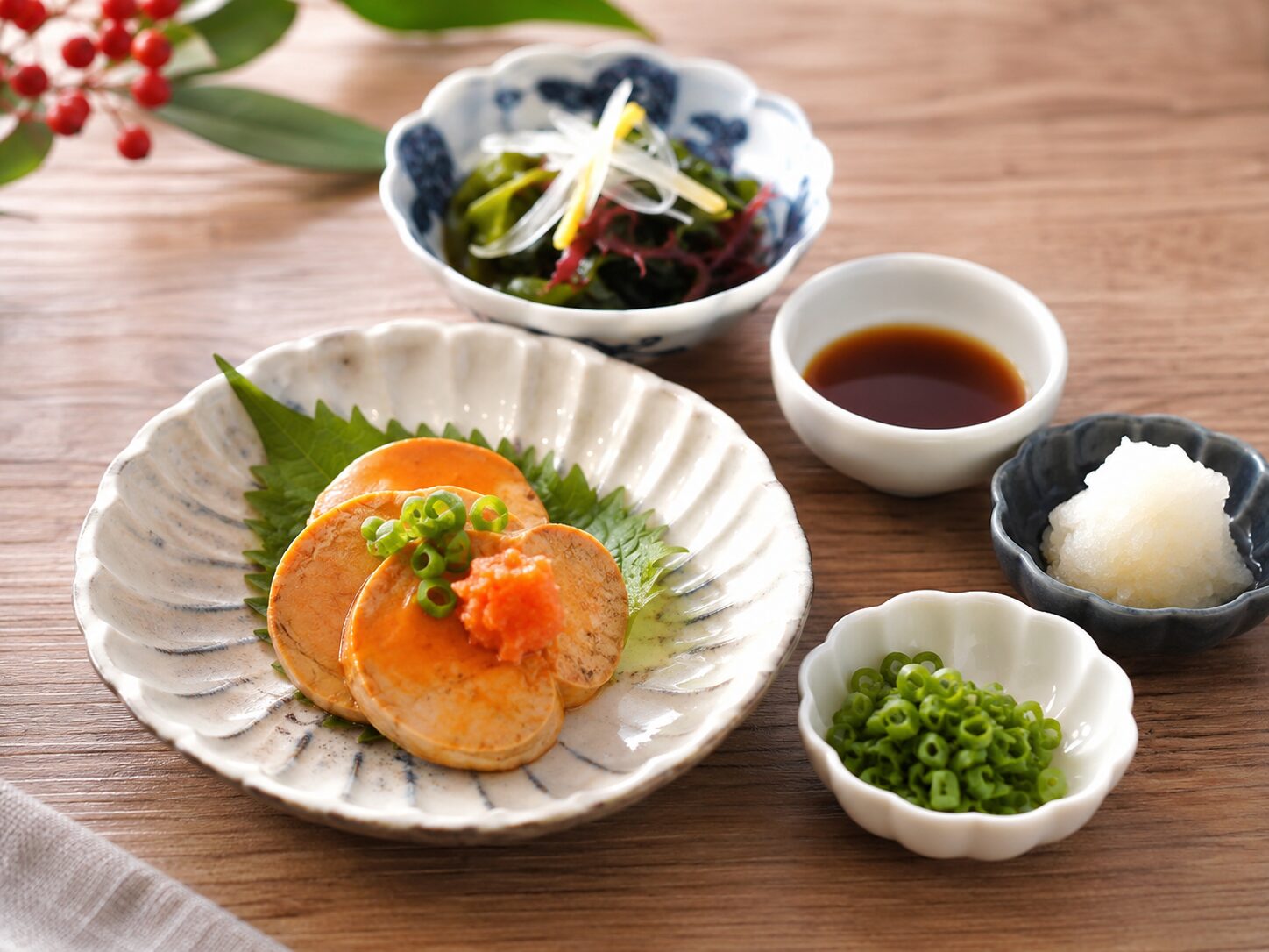 あん肝を小皿に少量盛り、ポン酢、大根おろし、小ねぎ、海藻サラダと一緒に食べる健康的な和食のイメージ。無料写真素材で、適量、薬味、野菜との食べ合わせが伝わる画像を使用する
