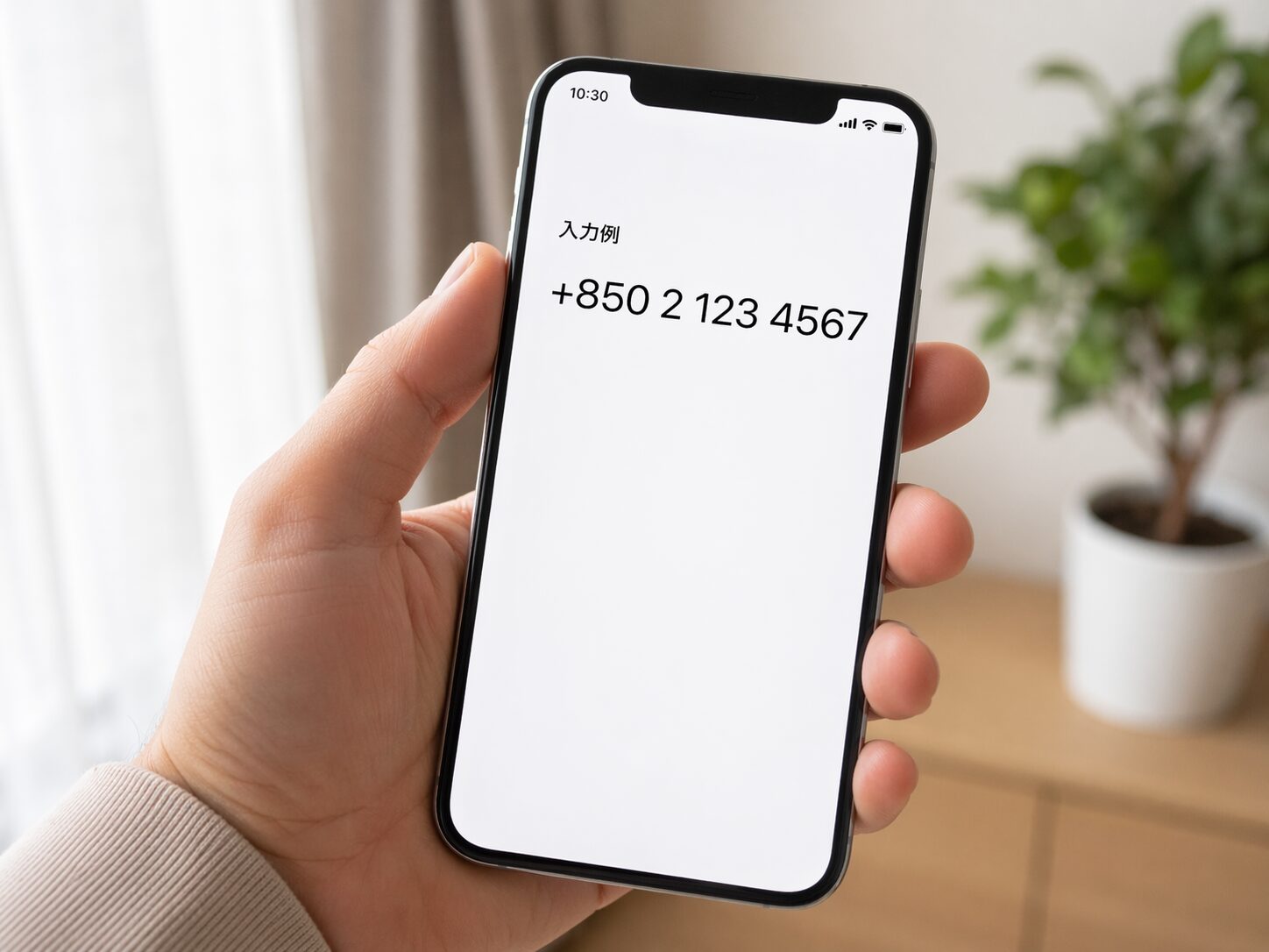 スマートフォンで国際電話番号の入力例としてプラス850から始まる番号を確認しているイメージ画像を配置。無料素材サイトでスマホ画面と手元が自然に写る写真を使用。