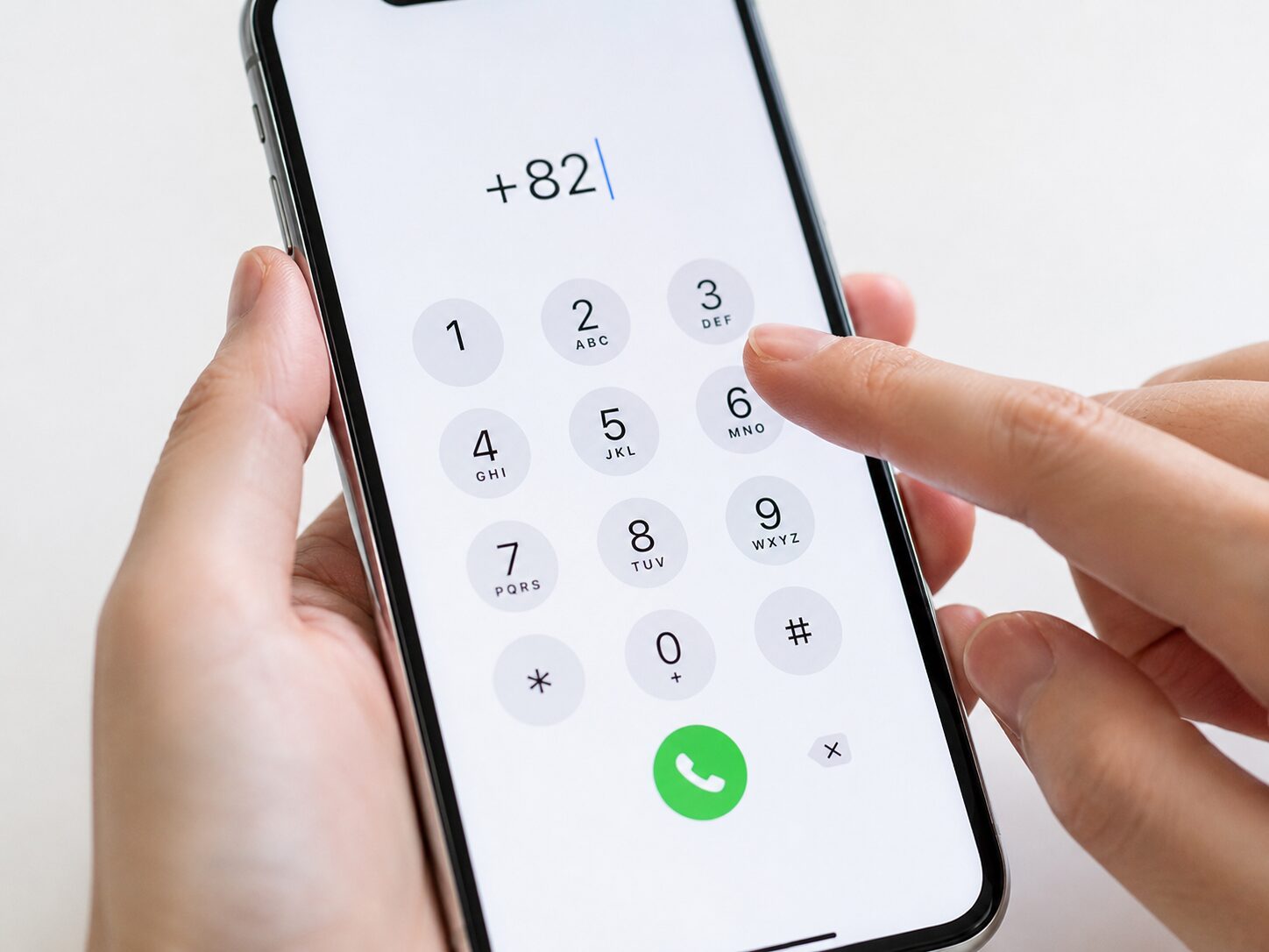 スマートフォンのダイヤル画面で海外電話用に+と国番号を入力している手元のイメージ