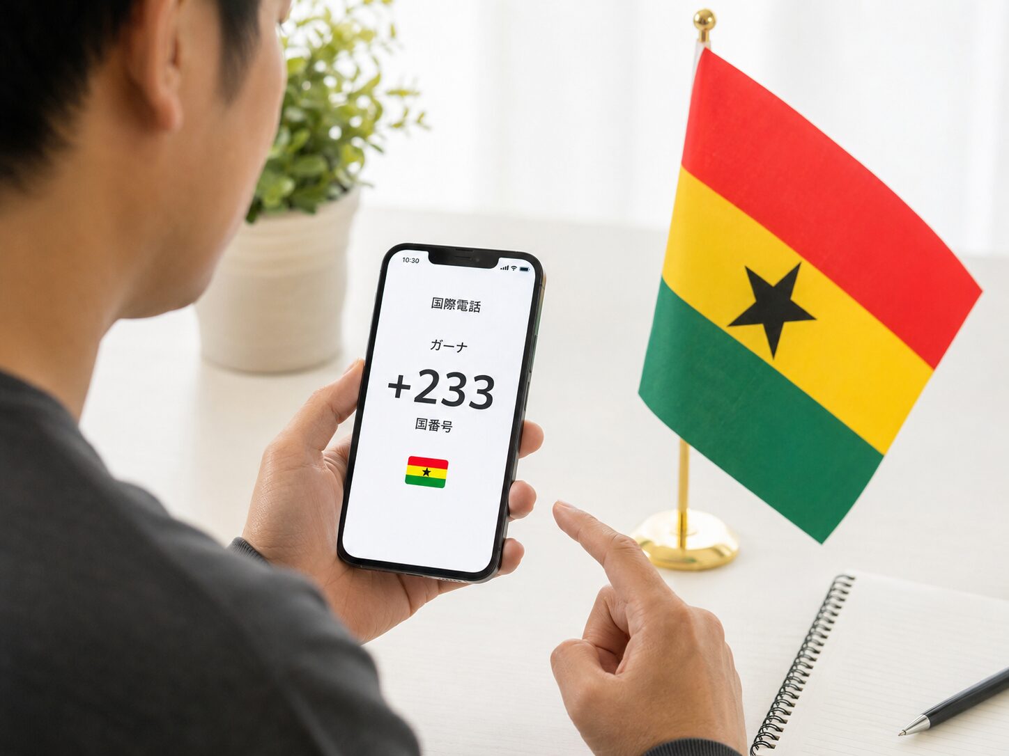 ガーナ国旗とスマートフォンを見ながら国番号+233を確認しているイメージ