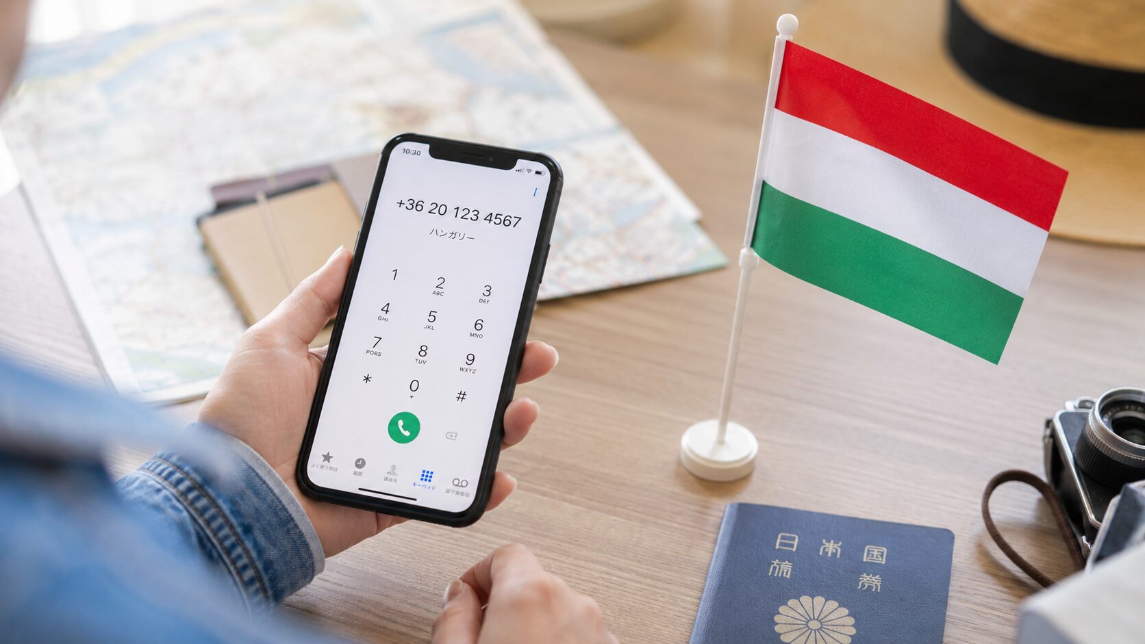 ハンガリーの国旗とスマートフォンを並べて国番号+36を確認している旅行者の写真