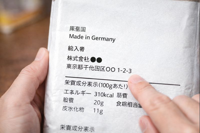 商品パッケージの原産国表示や輸入者情報を確認しているイメージ画像