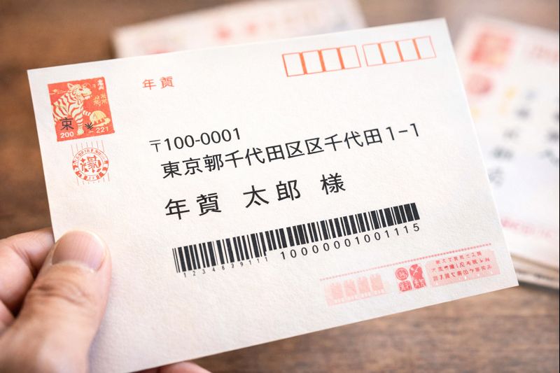 宛名面に印字されたカスタマバーコードの例が分かる無料素材（年賀状の宛名面を手元で確認しているイメージ）