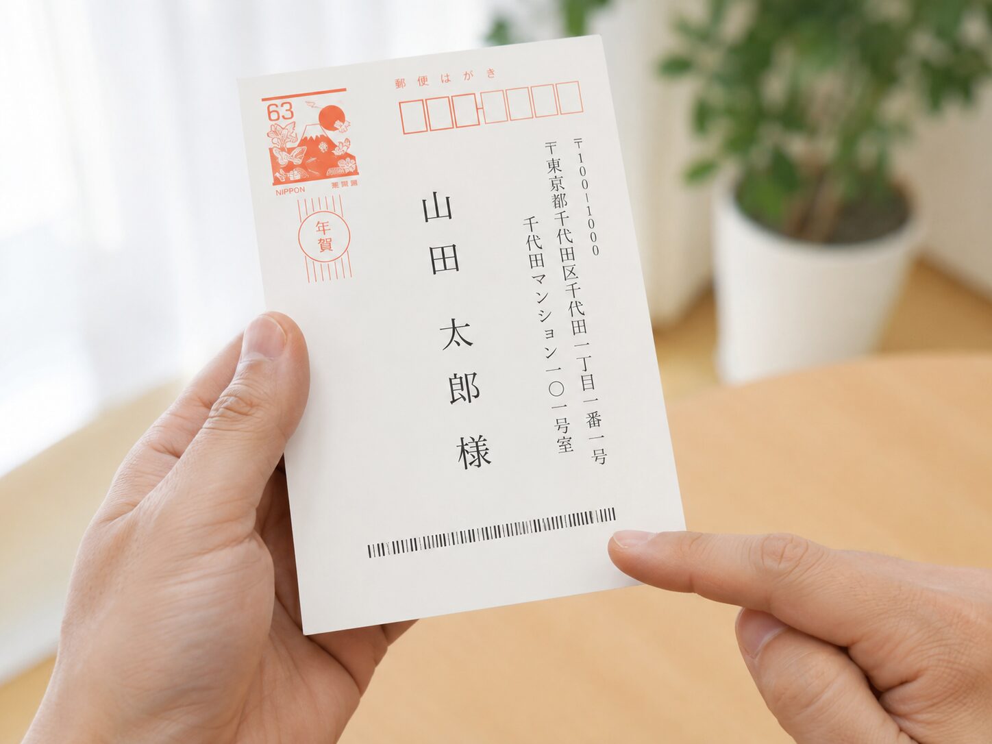 年賀状の宛名面に印刷されたカスタマバーコードを指で示しているイメージ。無料素材で、宛名印刷されたはがきと細いバーコードが分かる写真を使用する