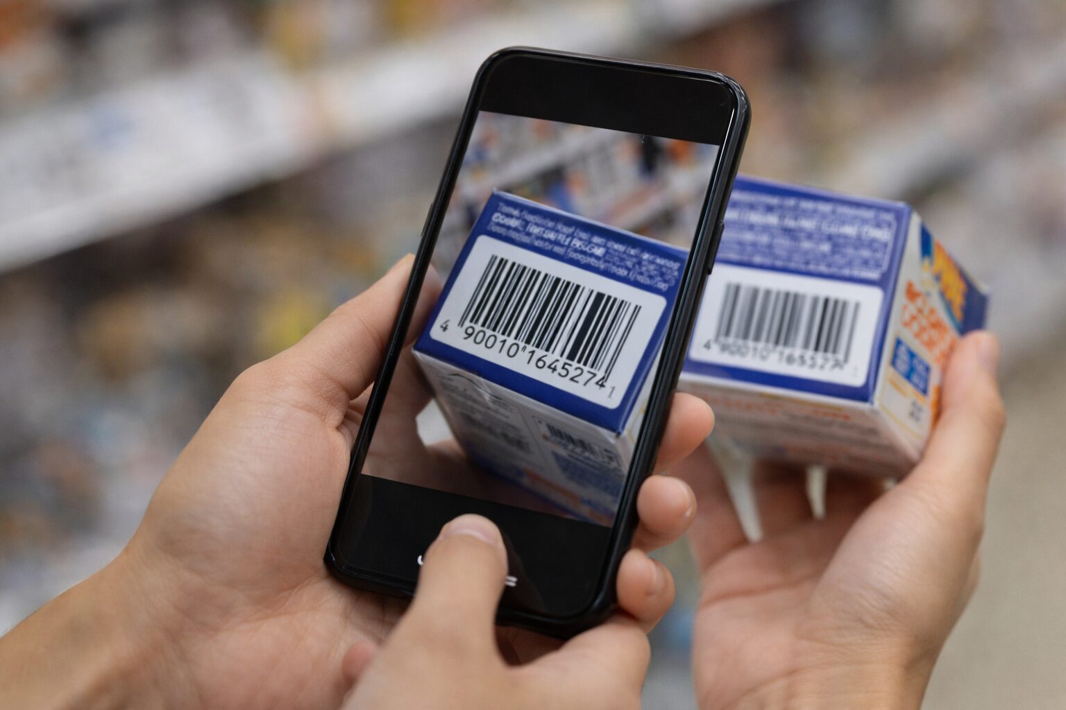 スマートフォンで商品バーコードを確認している日常シーン。手元に商品パッケージが写っている(無料素材向け)